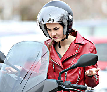 Vollkaskoversicherung Motorrad - Frau schaut verärgert auf ihr Motorrad